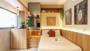 A modern hotel room with a wooden bed, a small kitchenette, a large window, and a view of the city. - Setin Pamplona R (Sao Paulo)