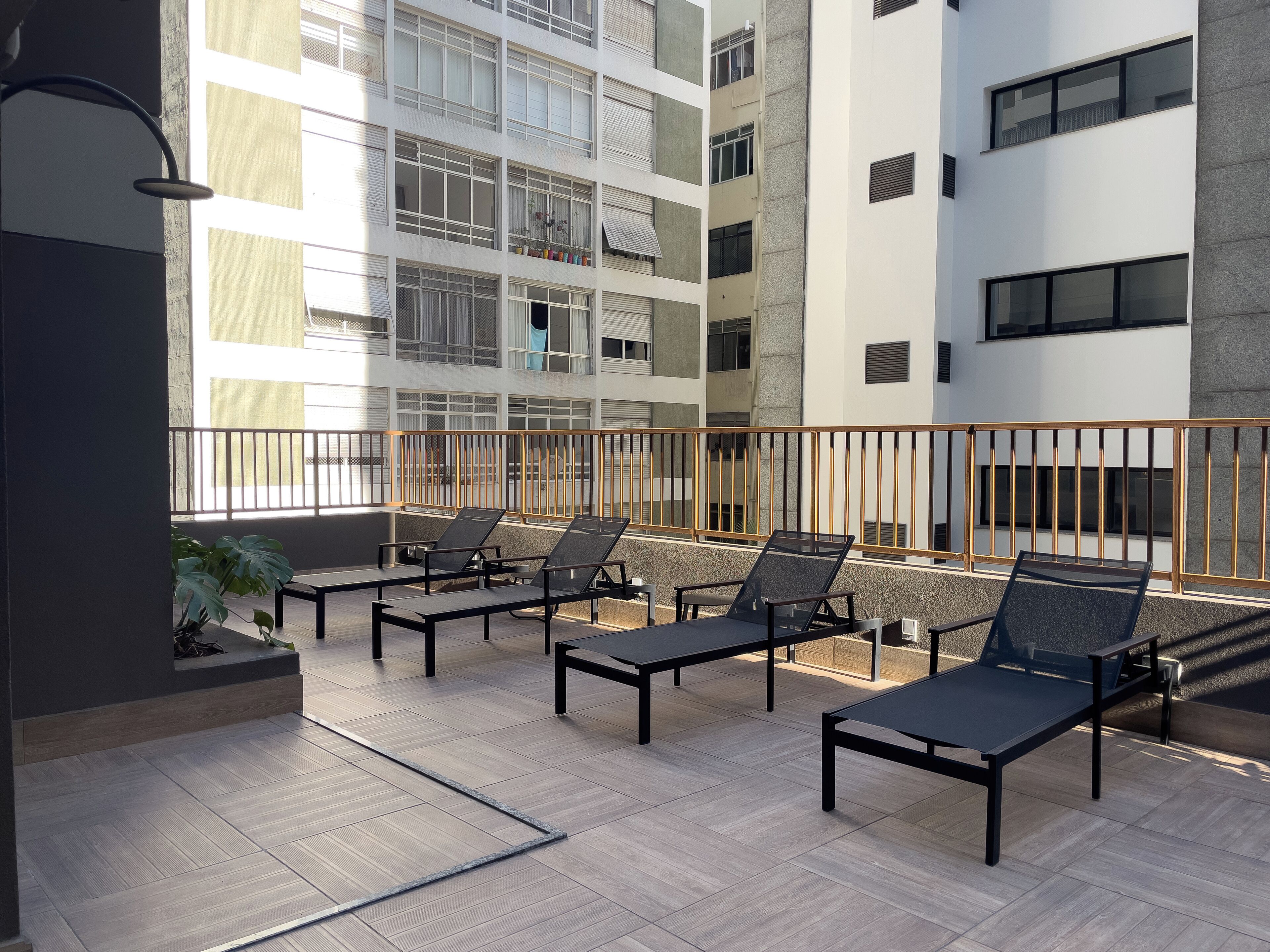A balcony with four lounge chairs, a potted plant, and a metal railing.