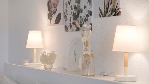 Een slaapkamer met een bed, nachtkastje met lamp, klok en wanddecoratie.