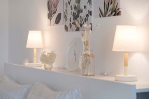 A bedroom with a bed, a bedside table with a lamp, a clock, and wall art.