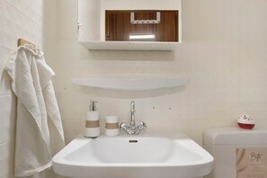 Une salle de bain avec un lavabo blanc, un porte-serviettes, un miroir et des toilettes.