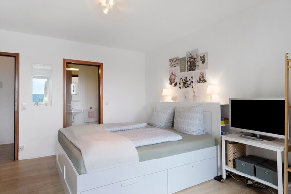 Une chambre à coucher avec un lit, des lampes de chevet, un téléviseur posé sur un meuble et des œuvres d’art accrochées au mur.