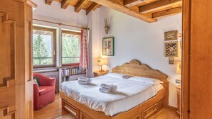 Une chambre confortable avec un lit en bois, un fauteuil rouge, une bibliothèque et une fenêtre avec des rideaux.