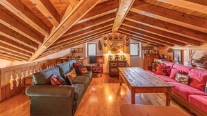 Une chambre mansardée avec des poutres en bois, un canapé, une table et un téléviseur.
