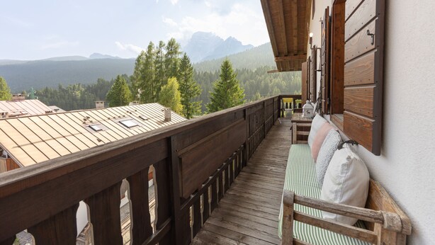 Un balcon en bois offrant une vue sur les montagnes et les arbres.