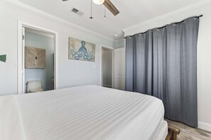 A bedroom with a bed, a ceiling fan, a painting, and a bathroom door. - Holiday Isle - Private Beach - Special Offer! (Destin)