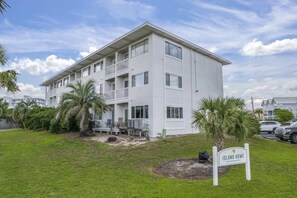 A multi-story building with balconies, a sign reading "ISLAND HOME," and a grassy area with palm trees. - Holiday Isle - Private Beach - Special Offer! (Destin)