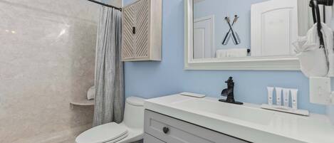 A bathroom with a shower, toilet, vanity with a mirror, and toiletries.