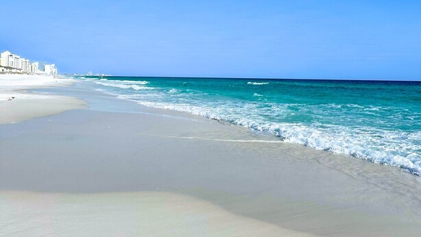 Ein Strand mit blauem Himmel, ruhigem Meer und Gebäuden entlang der Küste.