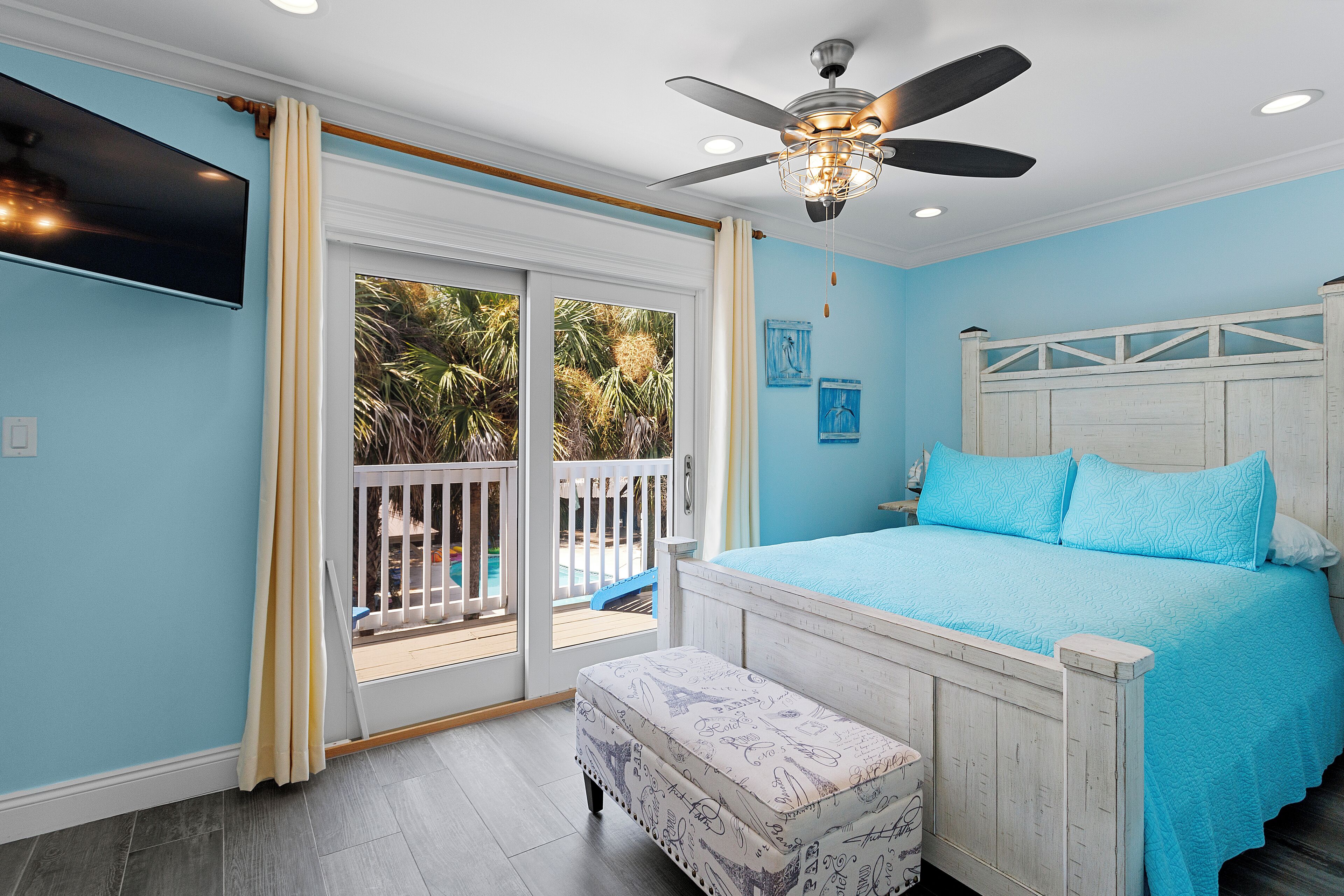 A bedroom with a bed, a ceiling fan, a TV, and a view of the outdoors.