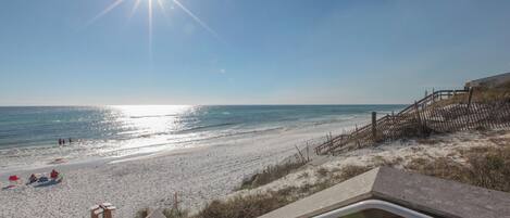 A beach with a wooden staircase leading down to the sand, a clear sky, and the ocean in the background.
