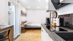Una cuina compacta amb zona de menjador, un llit i una finestra amb cortines de tela fina.