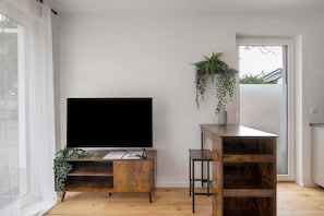 Ein Zimmer mit einem großen Flachbildfernseher auf einem Holzständer, einem kleinen Holztisch und einer hängenden Pflanze.