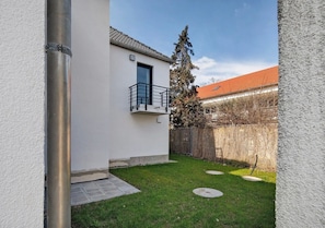A residential building with a balcony, a fenced yard, and a tree.