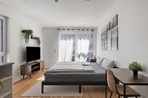 A modern bedroom with a bed, bedside table, TV, and a window with curtains. - Apartment “Ay Homes 08” with Balcony and Wi-Fi (Augsburg)