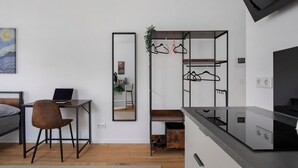 Una habitación moderna con una cama, un escritorio con una computadora portátil, un espejo, un perchero y una zona de cocina.