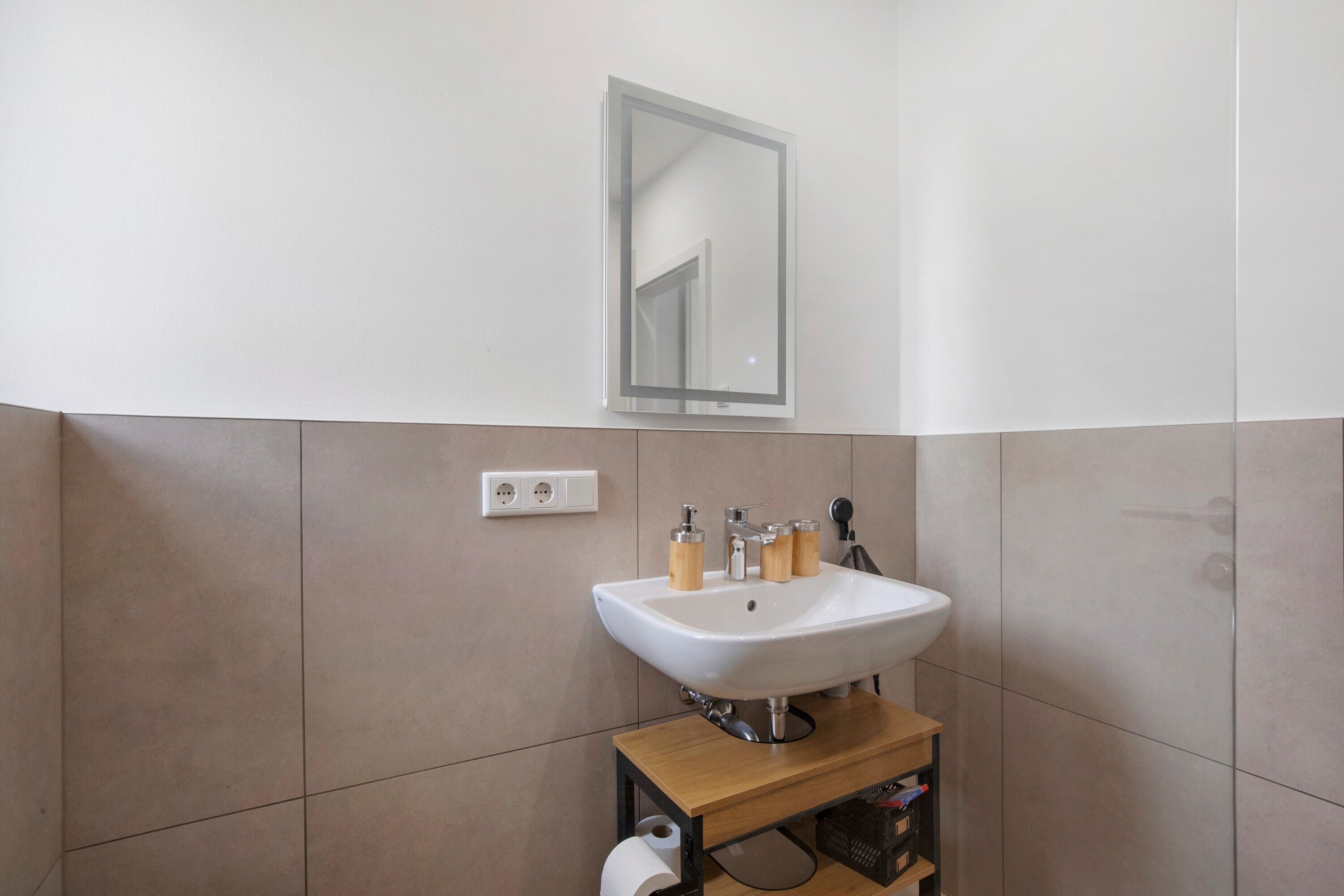 A bathroom with a white sink, mirror, and two light switches on the wall.