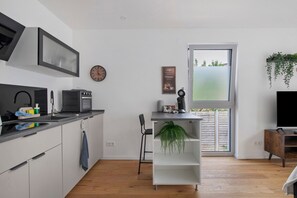 A modern kitchen with a microwave, sink, and a small dining area with a chair and a plant.