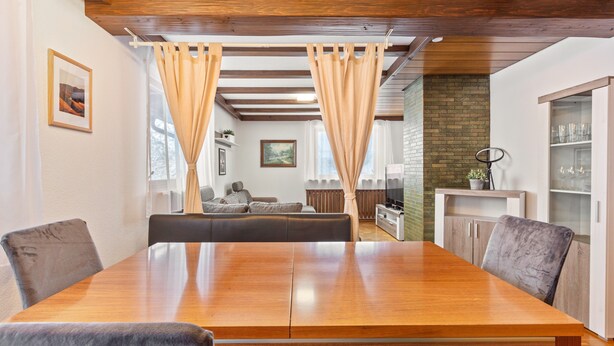 Un área de comedor con una mesa y sillas de madera, un sofá y una cocina al fondo.