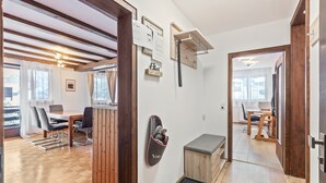 Una habitación con piso de madera, una mesa de comedor con sillas, un banco, un zapatero en la pared y una puerta que da a otra habitación.