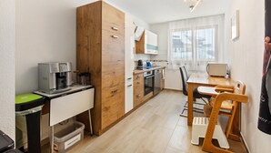 Cocina compacta con cafetera, microondas y tostadora. Hay una mesa de comedor con sillas y una ventana con cortinas.