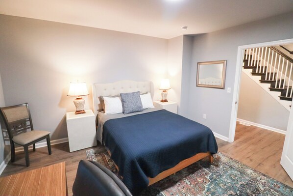 Une chambre à coucher avec un lit, des tables de chevet, une chaise, un tapis et un escalier.