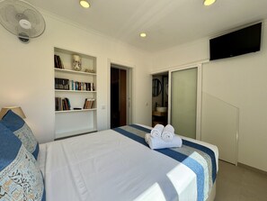 Een hotelkamer met een bed, een boekenkast, een televisie en een badkamer, zichtbaar door een open deur.