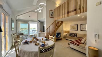Amplia sala de estar con mesa de comedor dispuesta para una comida, sofá y escalera que lleva a un nivel superior.