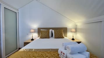 Une chambre d’hôtel avec un lit, deux tables de chevet, une commode, une fenêtre et une porte.