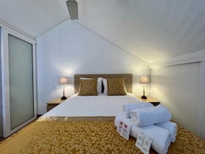 Une chambre d’hôtel avec un lit, deux tables de chevet, une commode, une fenêtre et une porte.