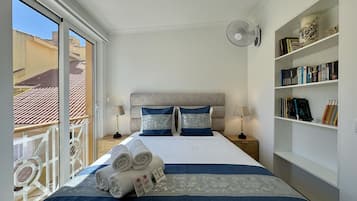 A hotel room with a bed, two bedside tables, a bookshelf, and a balcony with a railing.