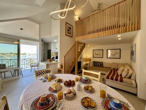 Un coin repas avec une table ronde dressée pour le petit-déjeuner, un escalier et une vue sur la mer.