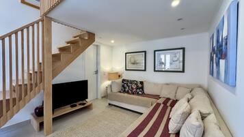 Een moderne woonkamer met een houten trap, een flatscreen televisie, een bank en twee ingelijste kunstwerken aan de muur.