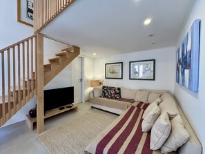 Un salon moderne avec un escalier en bois, un téléviseur à écran plat, un canapé et deux œuvres d’art encadrées accrochées au mur.
