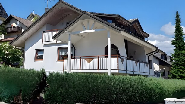 Una casa de dos pisos con balcón, antena parabólica y chimenea.
