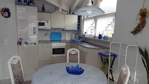 Una cocina con mesa, sillas, microondas, horno y una lámpara colgante.