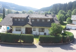 A two-story house with a tiled roof, a front door, and a small front yard with hedges.