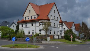 Un grand bâtiment à plusieurs étages, doté d’un toit recouvert de tuiles rouges, entouré d’un mur de pierre et d’une zone herbeuse.