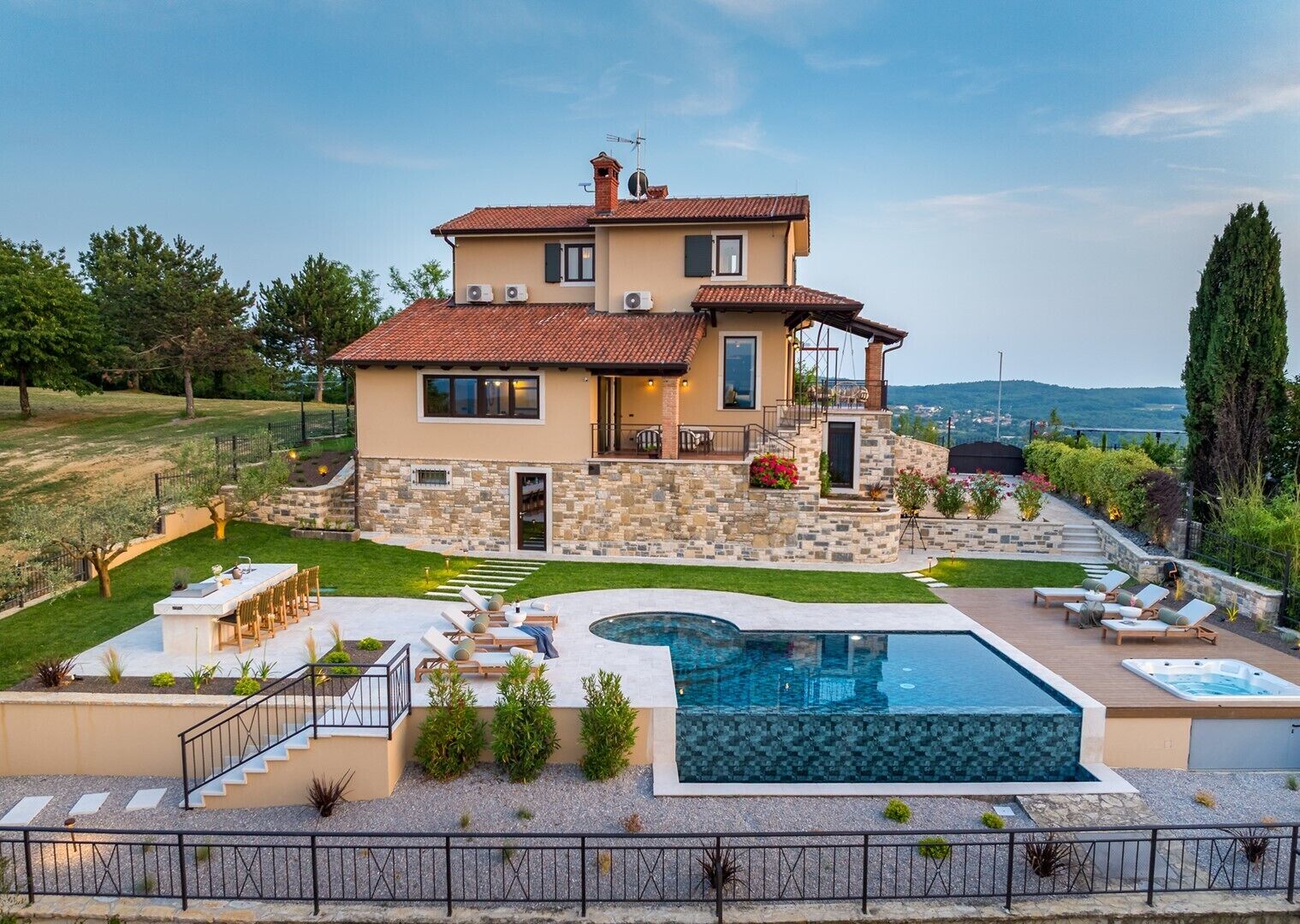 A two-story house with a stone facade, a swimming pool, and a patio with lounge chairs.