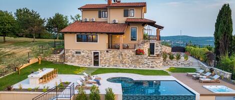 A two-story house with a stone facade, a swimming pool, and a patio with lounge chairs.