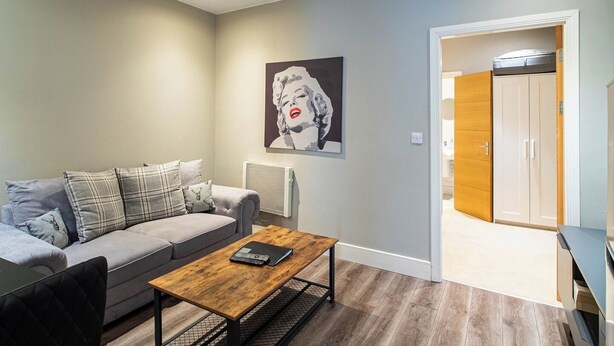 Un salon avec un canapé gris, une table basse en bois et un tableau accroché au mur.