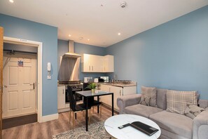 Een ruimtelijk ingerichte leefruimte met kitchenette, een eethoek en een zithoek met een bank en salontafel.