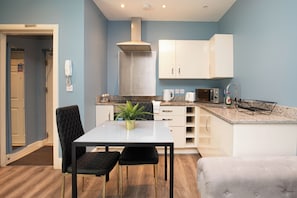A compact kitchen with a dining area, including a table with two chairs, a microwave, a kettle, and a sink with a dish rack.