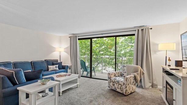 Un salon avec un canapé bleu, une table basse blanche, un fauteuil à motifs et une vue dégagée sur l’extérieur grâce à une grande porte-fenêtre coulissante.