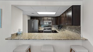 Une cuisine moderne avec des meubles de couleur sombre, des comptoirs en granit, des appareils électroménagers en acier inoxydable et un petit coin bar avec des tabourets.