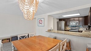 Une cuisine moderne dotée d’appareils électroménagers en acier inoxydable, d’un plan de travail en granit et d’un coin repas avec une table en bois et des chaises blanches.
