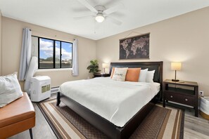 A hotel room with a bed, a desk, a chair, a heater, a window, and a world map on the wall.