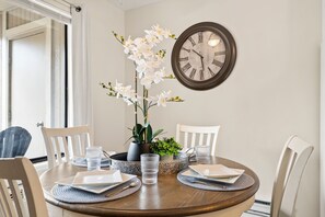 A dining table with chairs, a clock, and a vase of flowers.