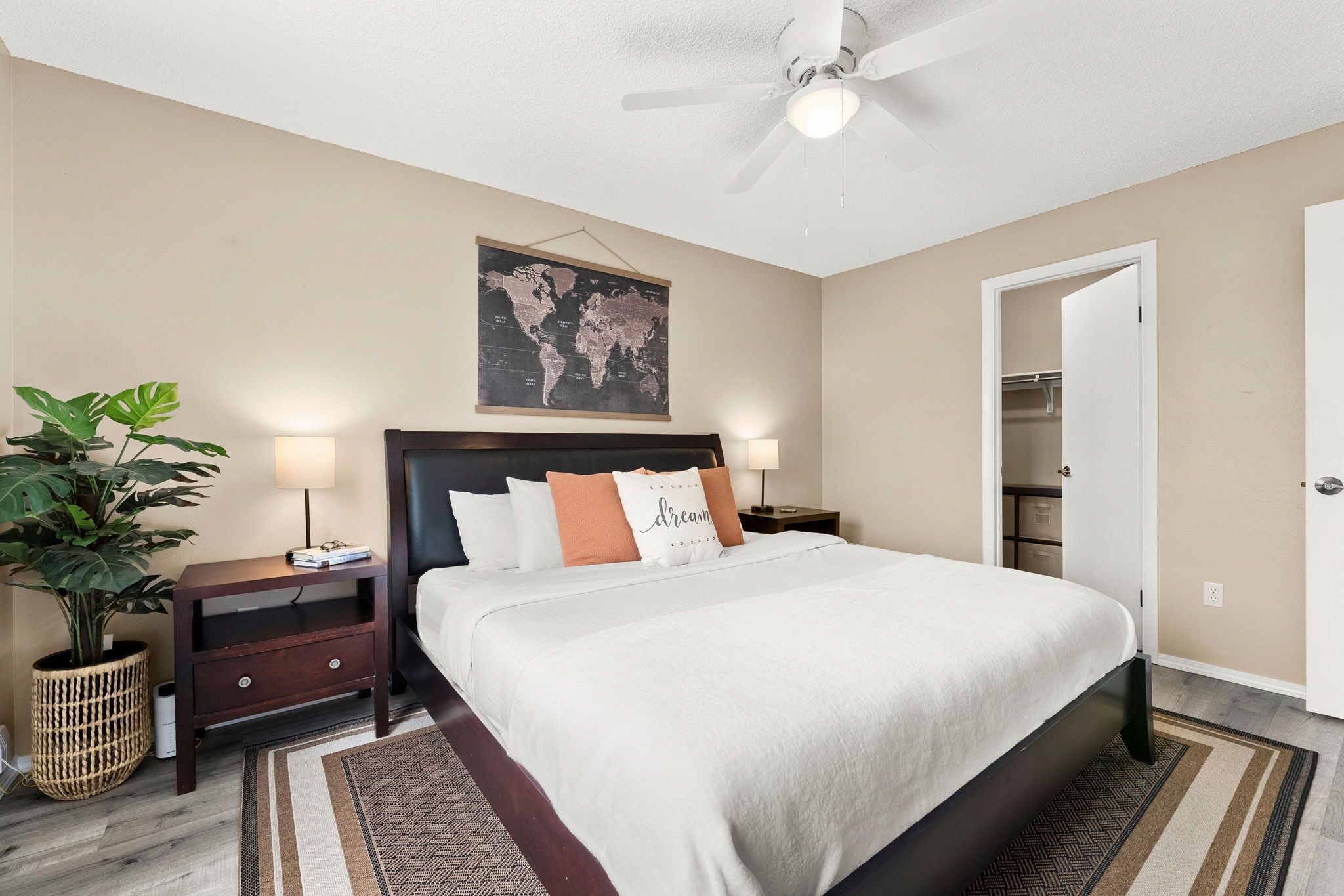 A neatly arranged bedroom with a bed, bedside tables, a world map, a ceiling fan, and a closet.