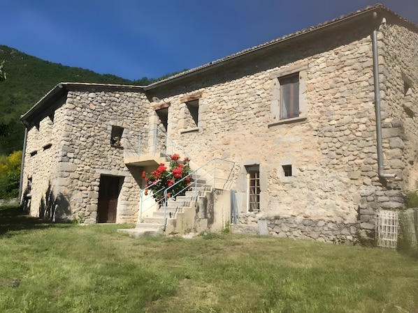 Edificio de piedra con una escalera que conduce a una puerta, rodeado de césped.